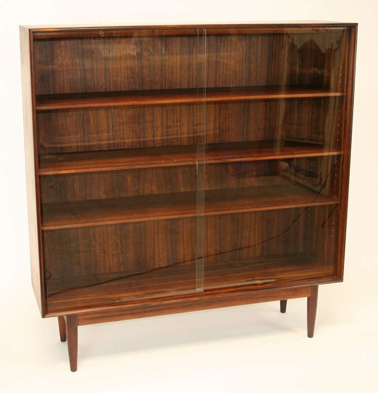 Bookcase on raised legs with sliding glass doors and three adjustable shelves in rosewood with lovely figuring. Can be used with or without glass doors. Finished back