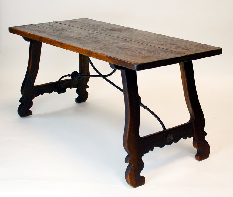 Walnut and wrought iron strap table with solid walnut top. Top was most likely one board but has split with age. carved lyre style legs, beautiful wrought iron stretchers. probably late 19th century, possibly 1910.