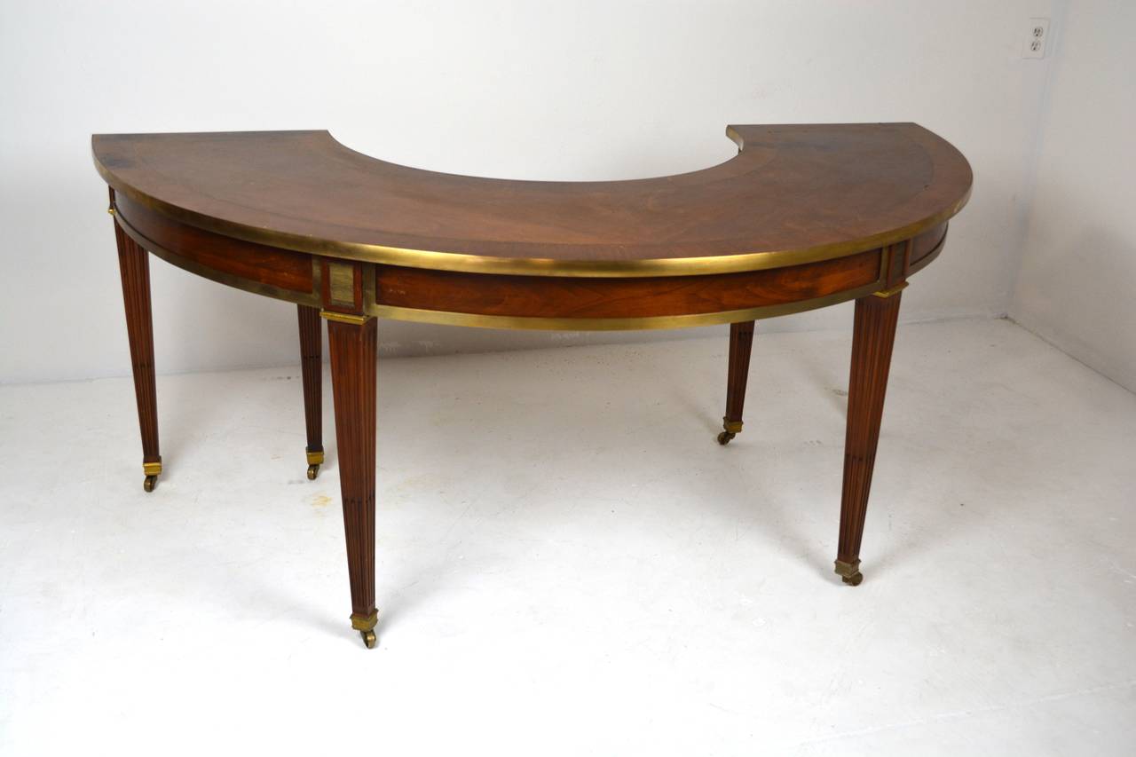 An elegant mid-century modern hunt table in the regency taste with central drawer. Bronze banded edges, inset brass plaques, with brass string inlay on top. Tapered reeded legs end in brass sabot and casters all in the manner of Jansen. Top has a