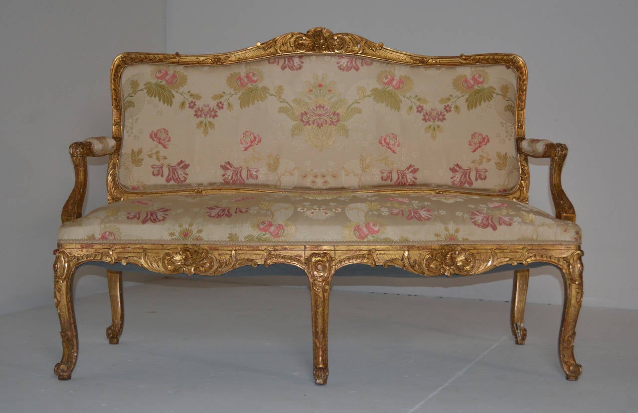 A French Louis XV style giltwood settee from the third quarter of the 19th century circa 1860-1880. The carved frame rests on cabriole legs with carved knees and gently scolled feet. The crest is centered with a rocaille. Acanthus wraps the