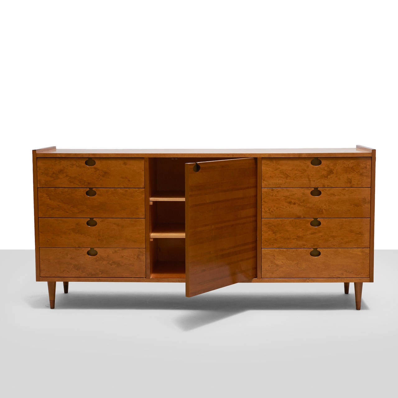 A wooden sideboard by Edmond J. Spence of maple with eight pull-out drawers and cabinet. Center section encloses storage area with three shelves and handle shaped trompe l’oeil cut-out with brass plate.