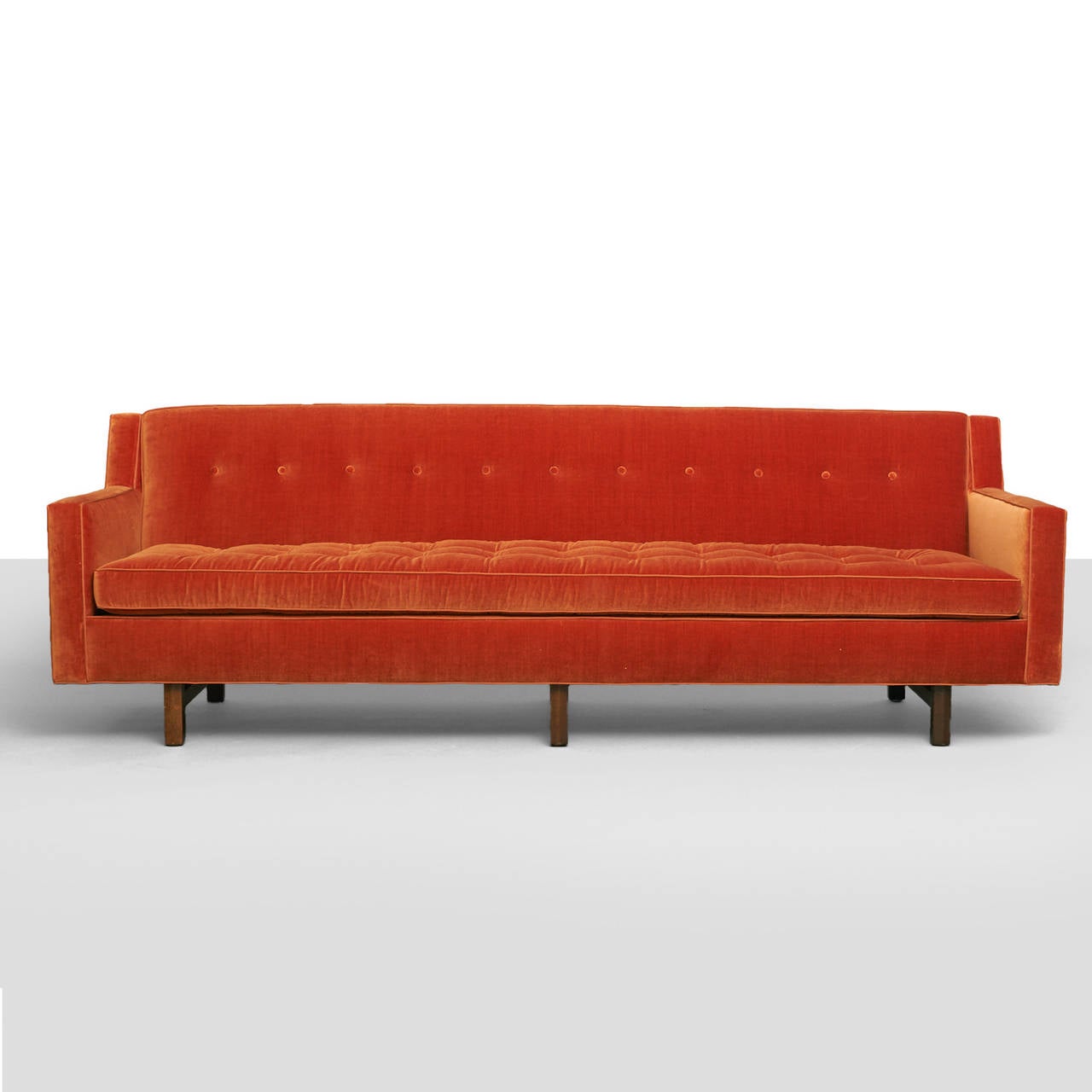 A long, tufted sofa by Edward Wormley recently restored in a George Spencer paprika color velvet with contrast silk trim and six mahogany legs.