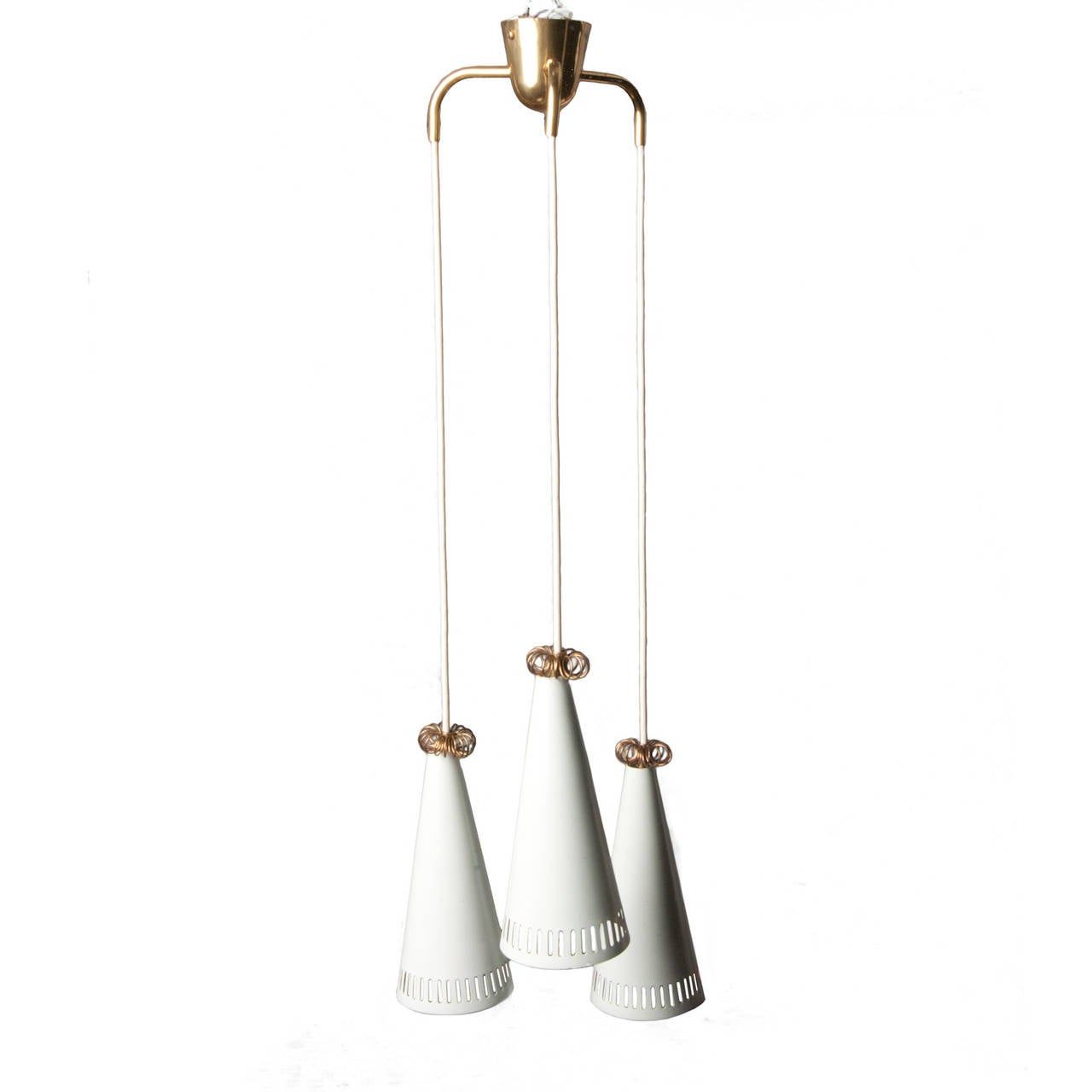 A three-pendant chandelier of brass and white enamel. Shades have a slotted metal detail and are topped with a curled brass ring.