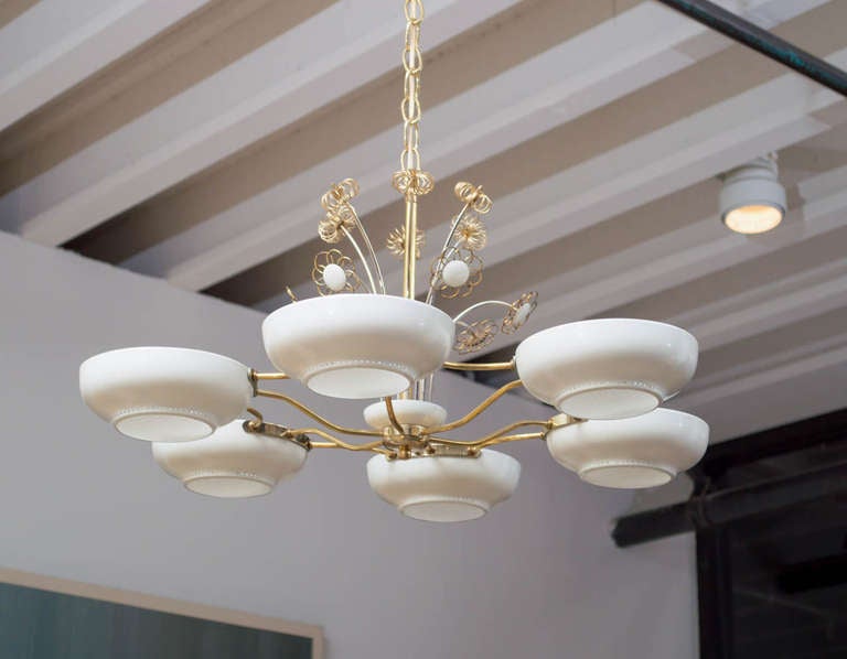 A pair of chandeliers by Paavo Tynell with six perforated white metal shades fixed with light diffusers connected by serpentine brass rods and topped by a fountain of white and brass daisies.