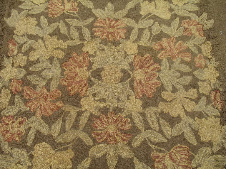 A large mid-20th century handwoven hooked rug featuring a oval floral palette in predominant soft brown. Other colors are earthy with soft rose and soft green accents,

circa 1940, measures: 11'3