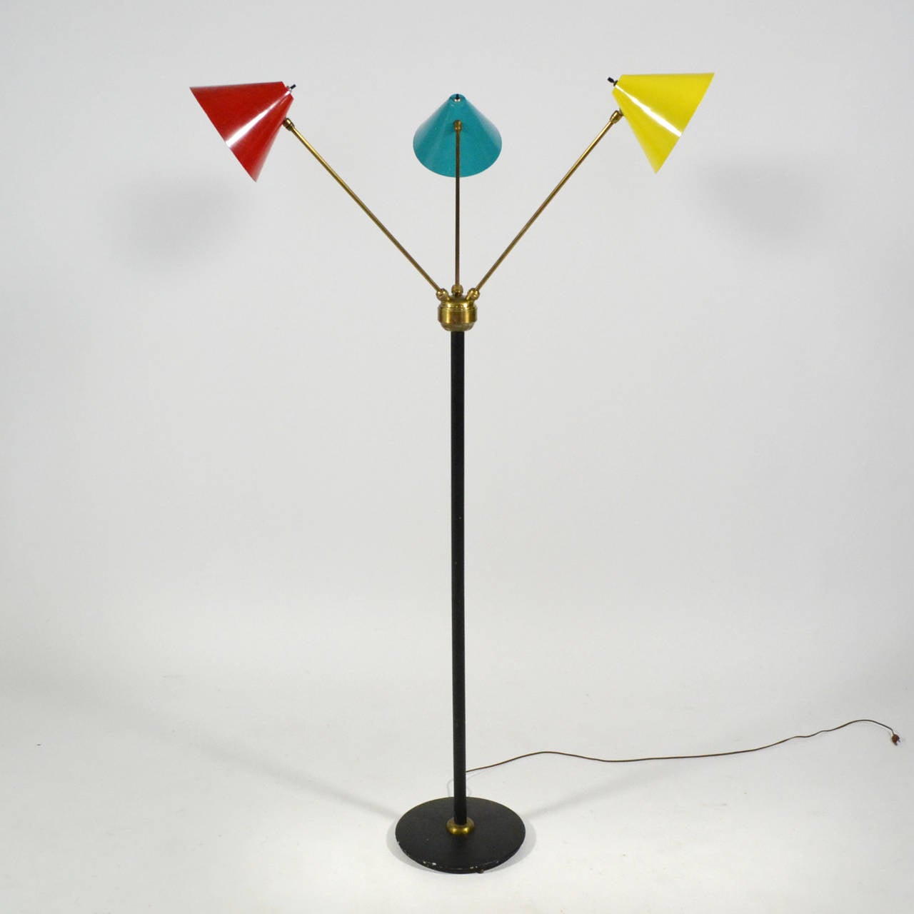 Diese dreiarmige Stehlampe ist ein wunderbares Beispiel für italienische Beleuchtung aus der Mitte des Jahrhunderts. Die konischen Schirme in Rot, Gelb und Blau sind mit Messingarmen an einem schwarzen zentralen Stiel und Sockel befestigt. Dank
