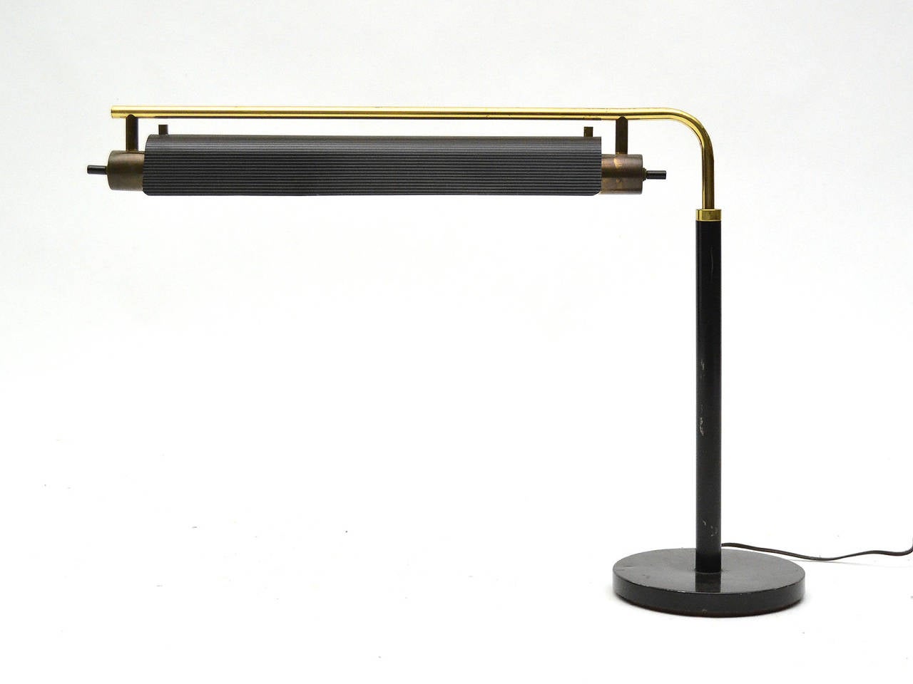 This Gerald Thurston desk or table lamp, has a shade which adjusts in height, swivels, and conceals two cylindrical bulbs which are switched independently. Combining brass and black enameled steel, the lamp has a stately presence.