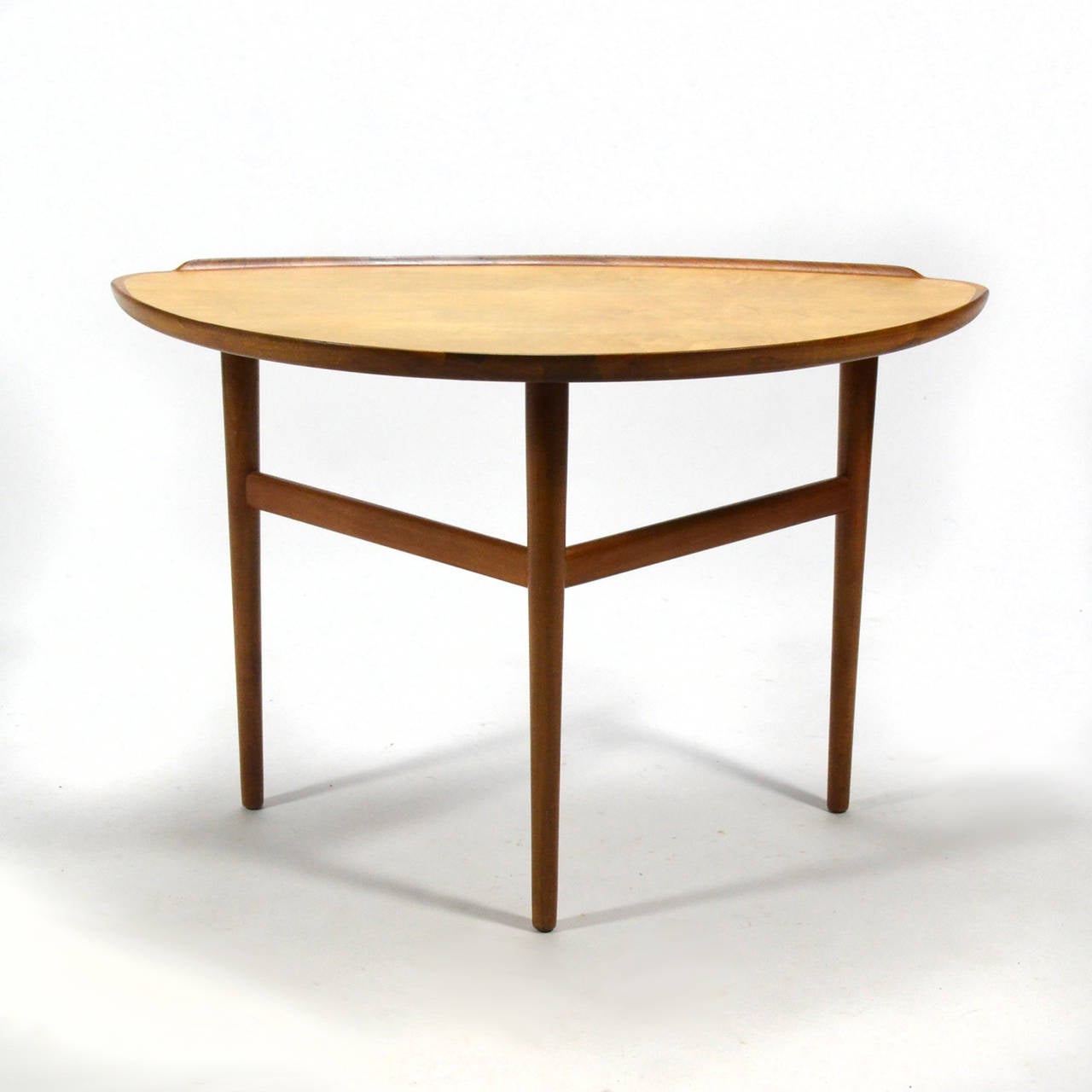 This beautiful table by Danish master Finn Juhl features solid walnut legs and raised lip that surrounds a delta-shaped top of sycamore. Designed during the peak of his creativity, this table is a perfect example of Juhl's aesthetic. Its scale