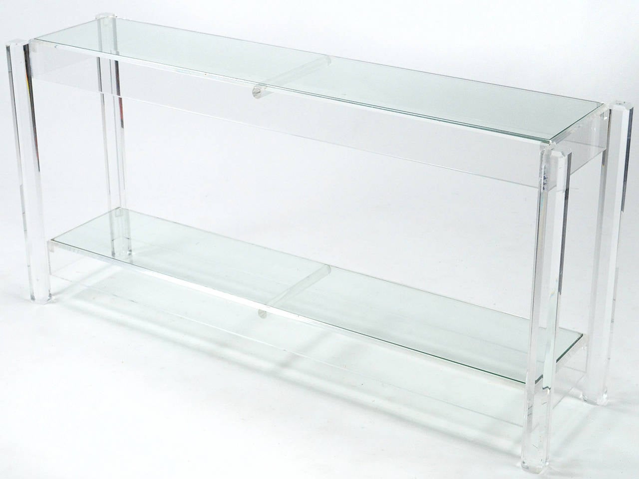 This two-tiered console or sofa table executed in Lucite with glass tops is handsome and understated. Beveled corners add depth to the faceted legs and skirts. Highly functional, the scale is perfect for an entryway or behind a sofa.