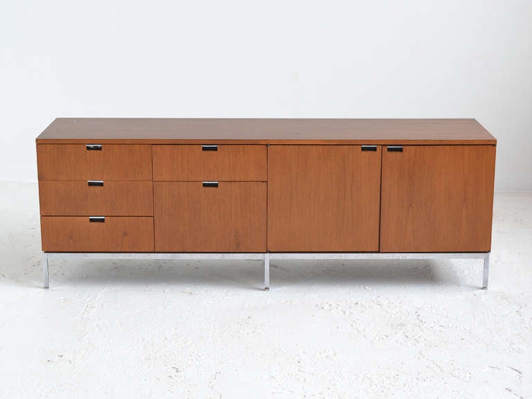 A classic design by Florence Knoll, this credenza in teak features a case fitted with four shallow drawers, one deep drawer, and two doors all with inset pulls supported by a polished chrome base.

We have two credenzas in this configuration and