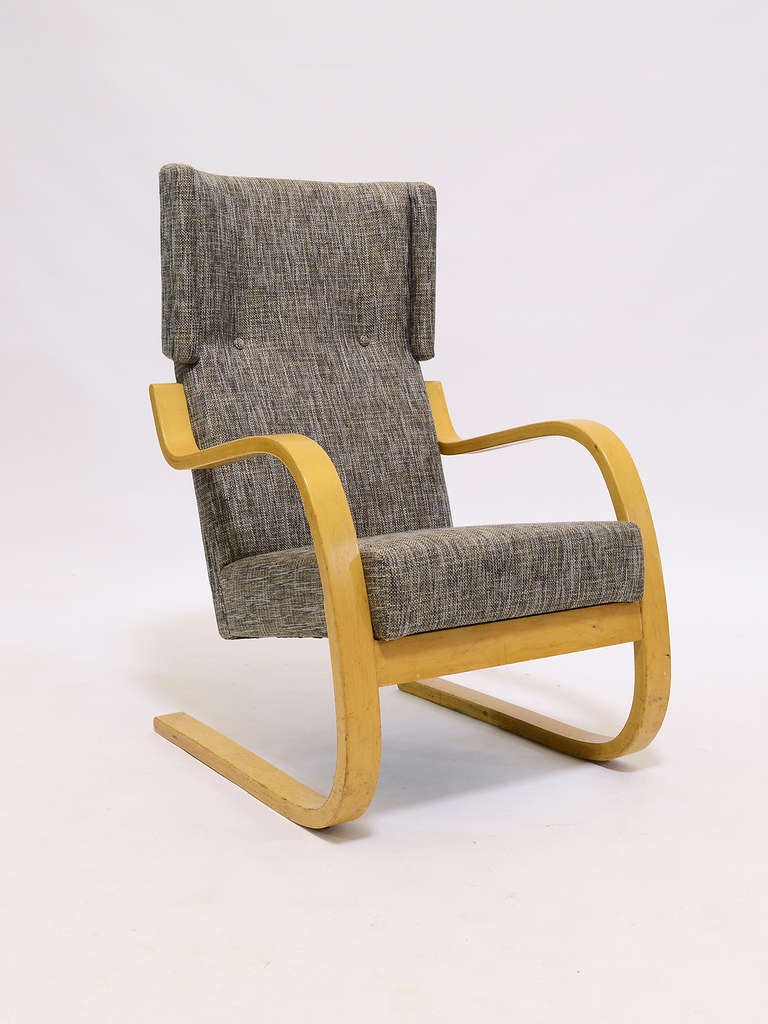 A classic design by the Finnish master Aalto, the cantilevered model 36 chair has a high, wingback. The beechwood frame cradles and supports the upholstered seat and back which are covered in a rich grey fabric with a coarse handwoven appearance.
