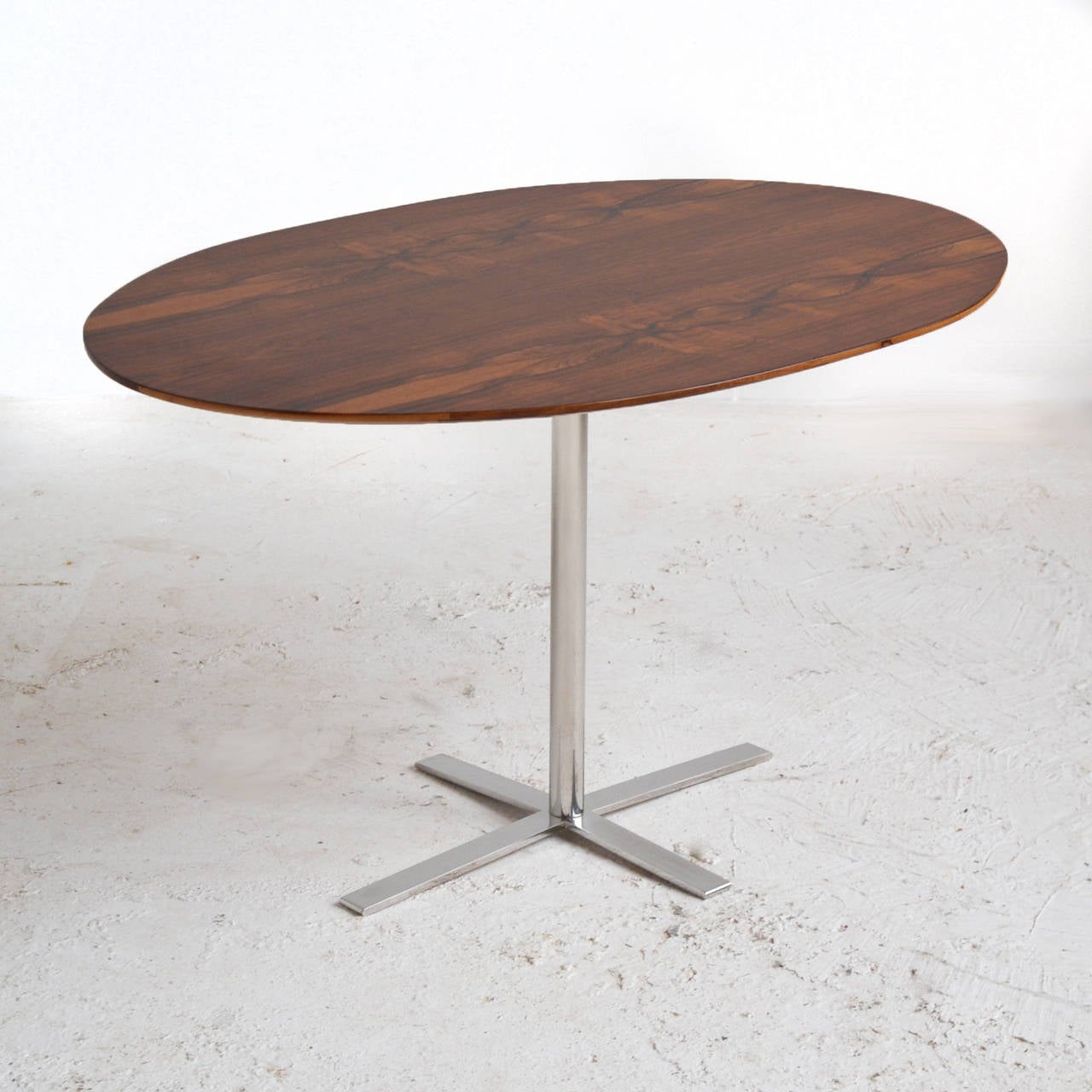 This attractive table features a beautiful oval rosewood top supported by a chrome base with cruciform shaped feet. We have been unable to definitively attribute this piece, but the sophisticated design reminds us of the work of  Arne Jacobsen, Ward