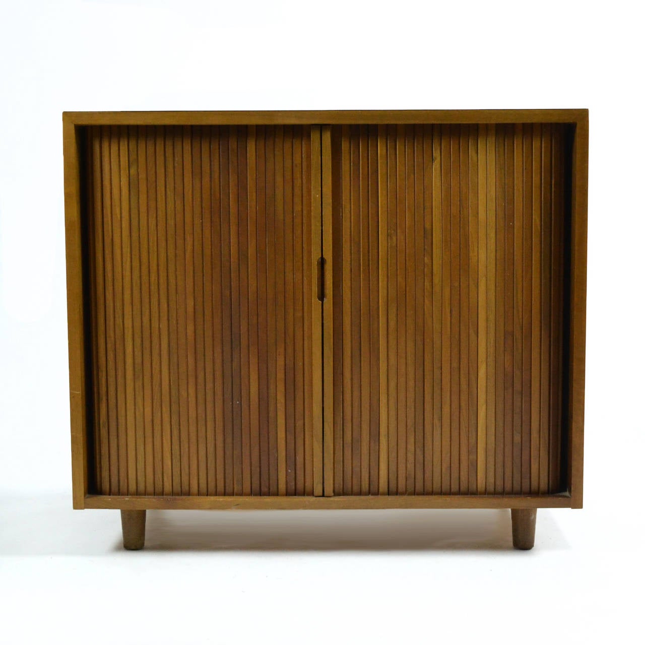 From a series of case goods designed for Glenn of California by Milo Baughman, this handsome walnut chest features two tamboured doors which conceal three drawers with bittersweet red drawer fronts, and a pull-out shelf perfect for folding and