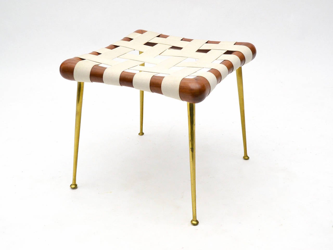 An exceptional design by Robsjohn-Gibbings, this stool has a seat of walnut and woven webbing supported by long tapered brass legs. Exquisitely crafted by Widdicomb, the heft of the piece belies the light, airy design.