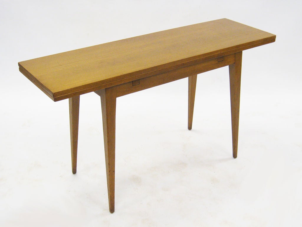 This table typifies Edward Wormley’s subtle and versatile design. Model number 4910 table has a top that slides forward and flips back to double in depth (from 17” to 34” ), converting from a console table to a dining table. 

Made by Dunbar, it