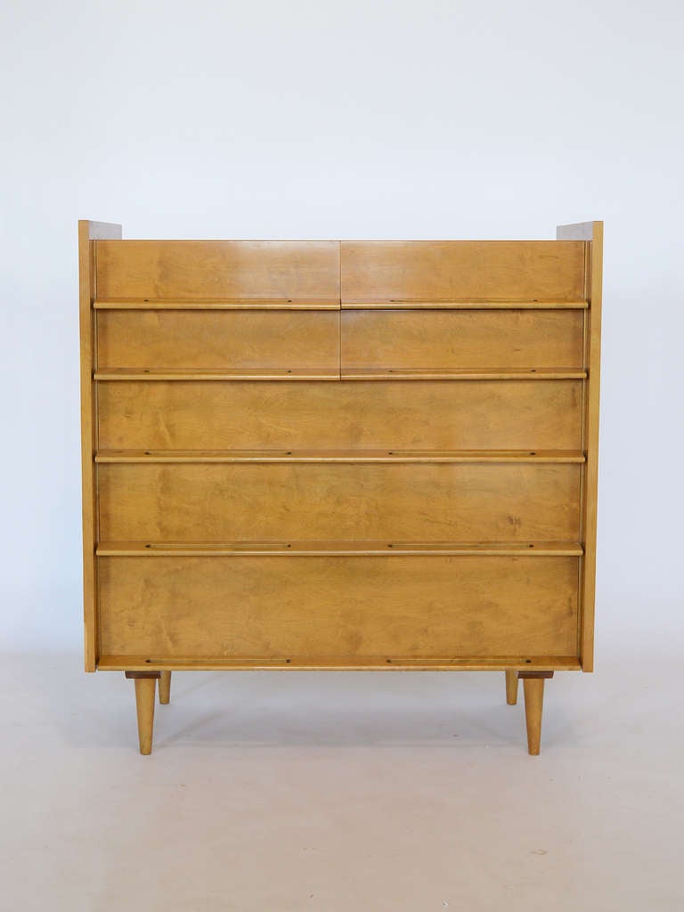 A refined and striking design by Edmond Spence, this dresser has a cabinet with raised sides and sculptural integrated drawer pulls that is supported by conical legs. 

Also available is a matching low dresser and a pair of nightstands.