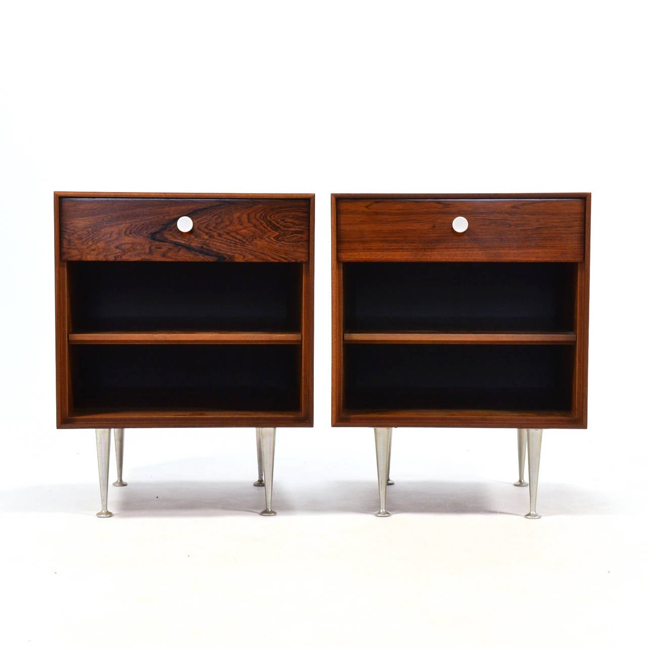 An exceptional pair of nightstands from Nelson's thin-edge rosewood group for Herman Miller, these lovely pieces are clad is highly figured rich rosewood. They feature the Classic white hourglass-shaped pulls and turned aluminum legs. 

Nelson