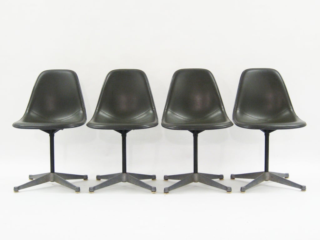 This set of side chairs by Charles and Ray Eames are post-war classics. The seats are elephant hide gray fiberglass with olive green naugahyde upholstery and they sit on cast aluminum four-star swivel bases. 

We also have a matching table available