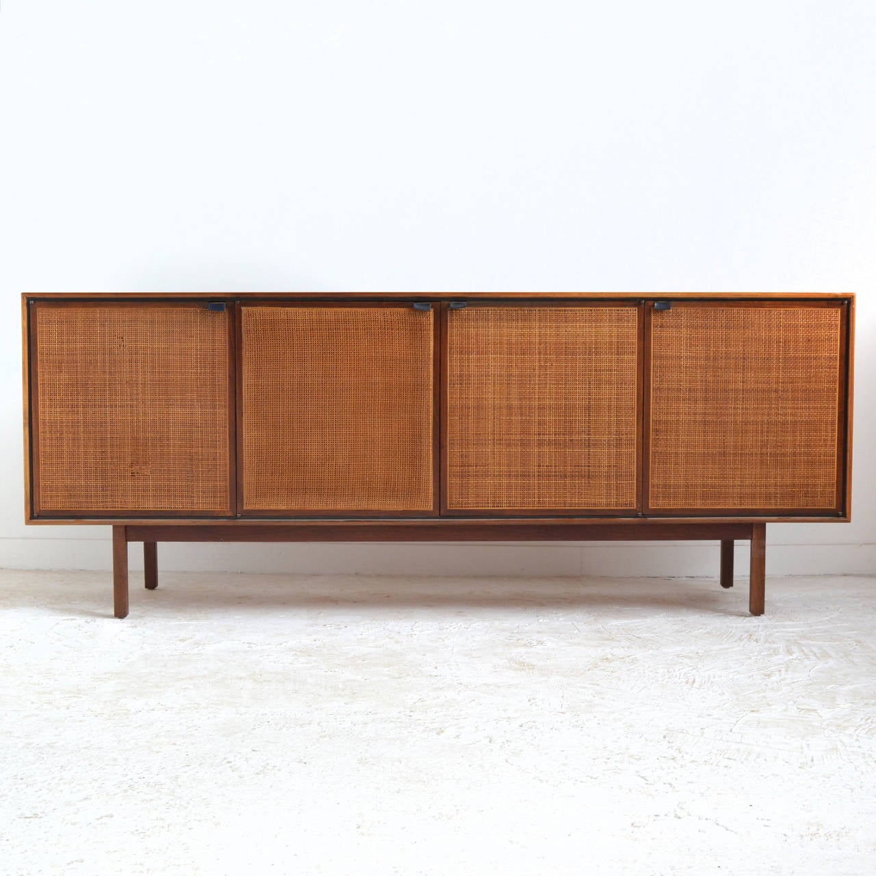 A beautifully designed and constructed credenza by Founders Furniture, it features a teak case with cane front doors and leather tab pulls supported by a rectilinear base. Doors conceal two adjustable shelves and two lined drawers

Included is a