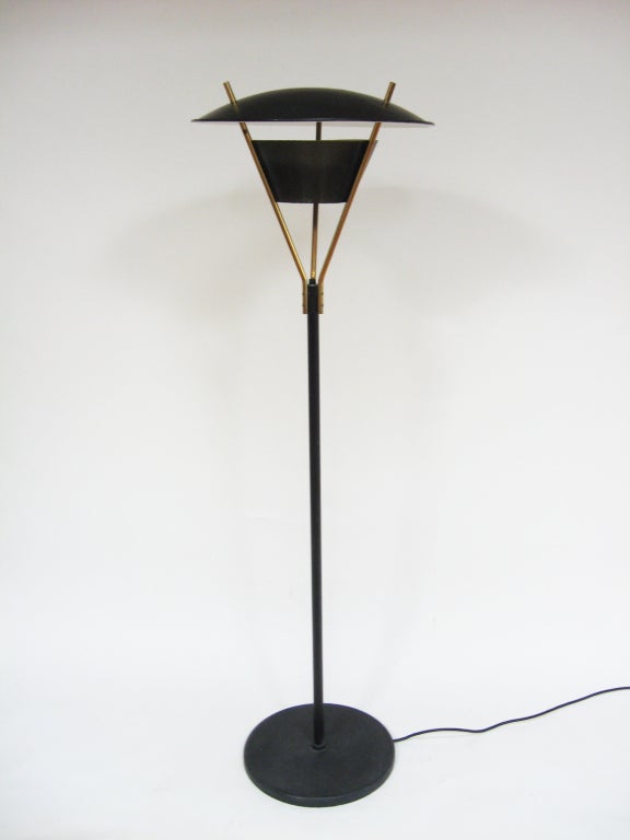 Questa grande lampada da terra è architettonica con una sobria giocosità, utilizza materiali innovativi (acciaio perforato) e luce riflessa per un bel mix di illuminazione diretta e indiretta. L'interruttore si trova in cima allo stelo nero, dove si