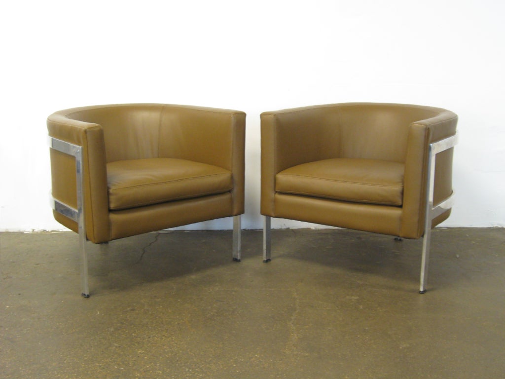 This attractive pair of barrel backed lounge chairs by Erwin-Lambeth are striking for their external aluminum frame which is supported by three legs. The new upholstery is a cafe con leche colored leather.