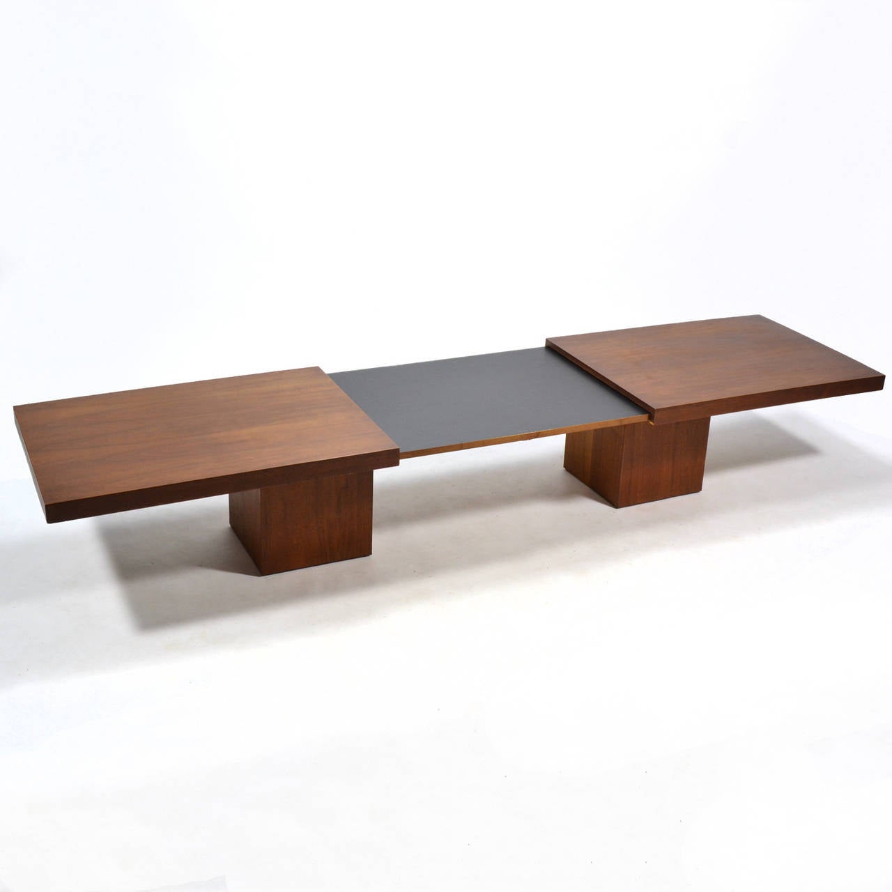 This beautiful design by John Keal is both handsome and versatile. The rectilinear top sits on a pair of cube bases offering a minimalist aesthetic… with a twist. The top is in two halves which separate and expand to reveal a center section of black