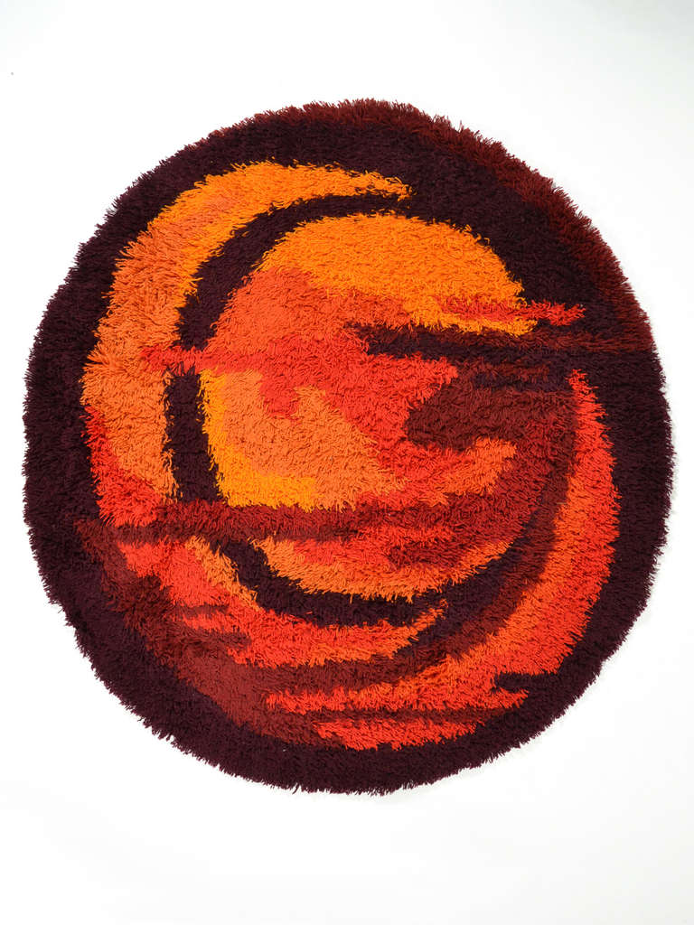 This terrific Rya rug is uncommon for its elliptical shape and fantastic condition, having been used by its original owner as a wall hanging rather than a floor carpet. The abstract design is executed in shades of orange, red and umber. The size