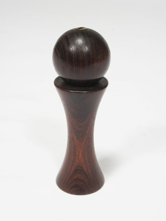 The sublime form of this peppermill is accentuated by grain of the rich solid rosewood. The hourglass shaped body is topped by a round handle that is attached to the grinder mechanism with a slotted metal fastener. The mechanism is a Peugeot which