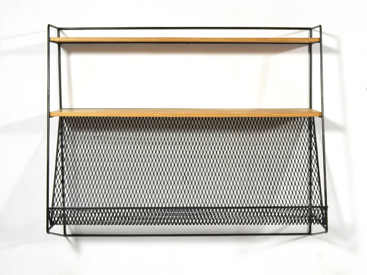 This wall-mounted shelf is quite similar to designs by Paul McCobb for Bryce. It has two solid shelves and a metal mesh magazine shelf for a light, airy and graphic quality.