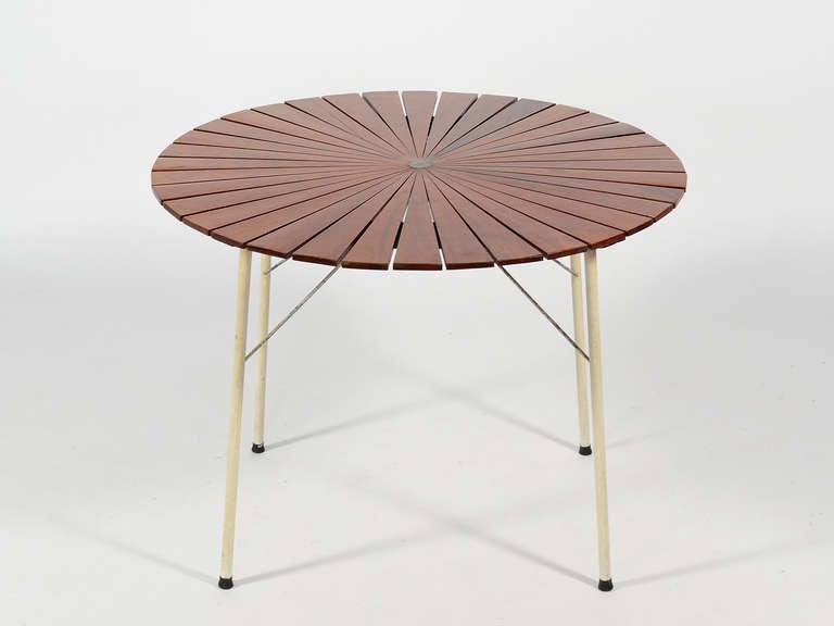 This lightly scaled table is fun, functional, and a visual delight. The round teak top is segmented in a star-burst pattern which not only lends visual interest, but allows it to be used outdoors where rainwater can run off in the gaps. The base is