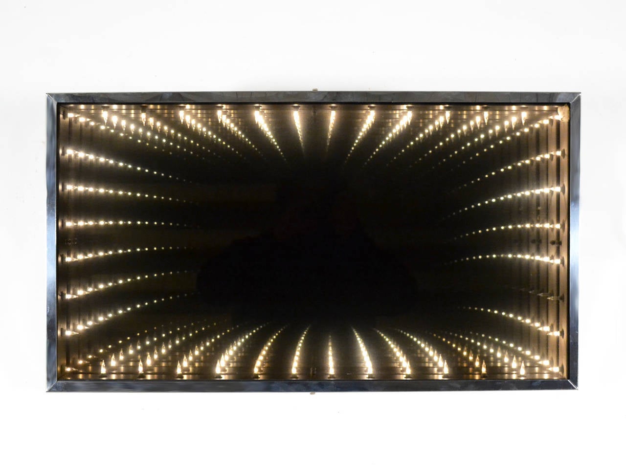 This compelling piece is both mirror and artwork. A two-way mirror set in a deep frame in front of a surround of tiny lights which, when illuminated, create the illusion of great depth.