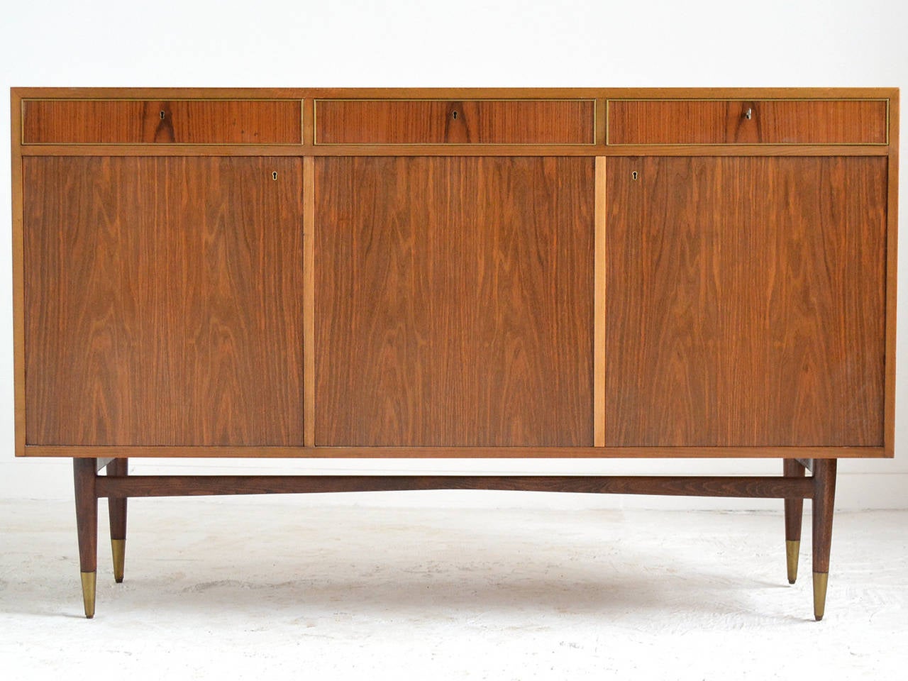 This Italian credenza or bar is a stunning piece. Perched on slender tapered legs with brass caps, the case is clad in a beautiful mix of woods. It appears to be a combination of Italian walnut, fruitwood, and mahogany. There are a number of