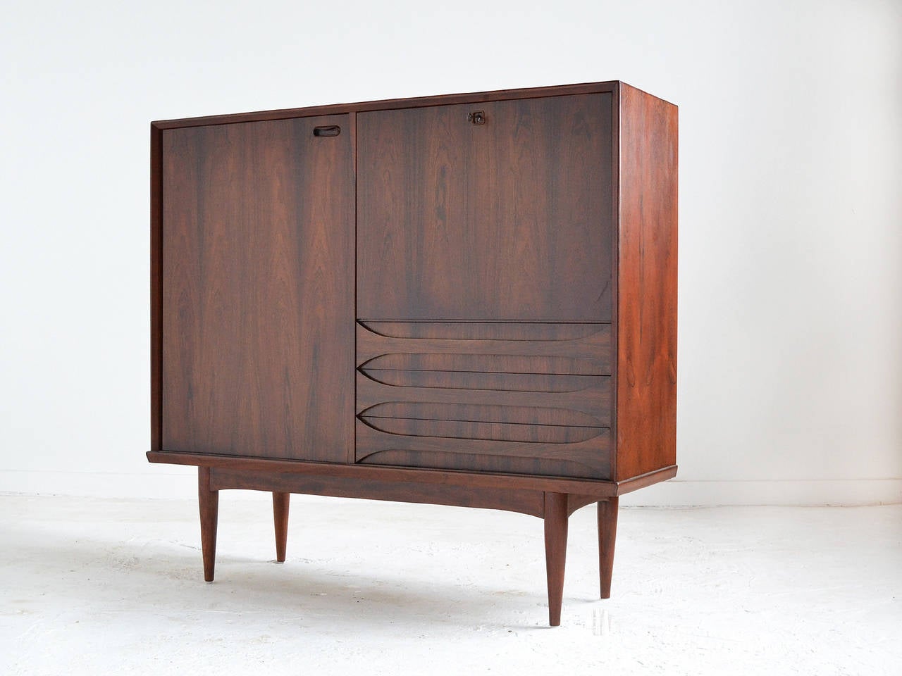 A stunning piece that garners attention in any room, this tall chest or bar by Arne Vodder is made of rich, highly figured rosewood. It has two doors (one of which locks) that conceal four oak shelves and a bank of three low drawers. The case is