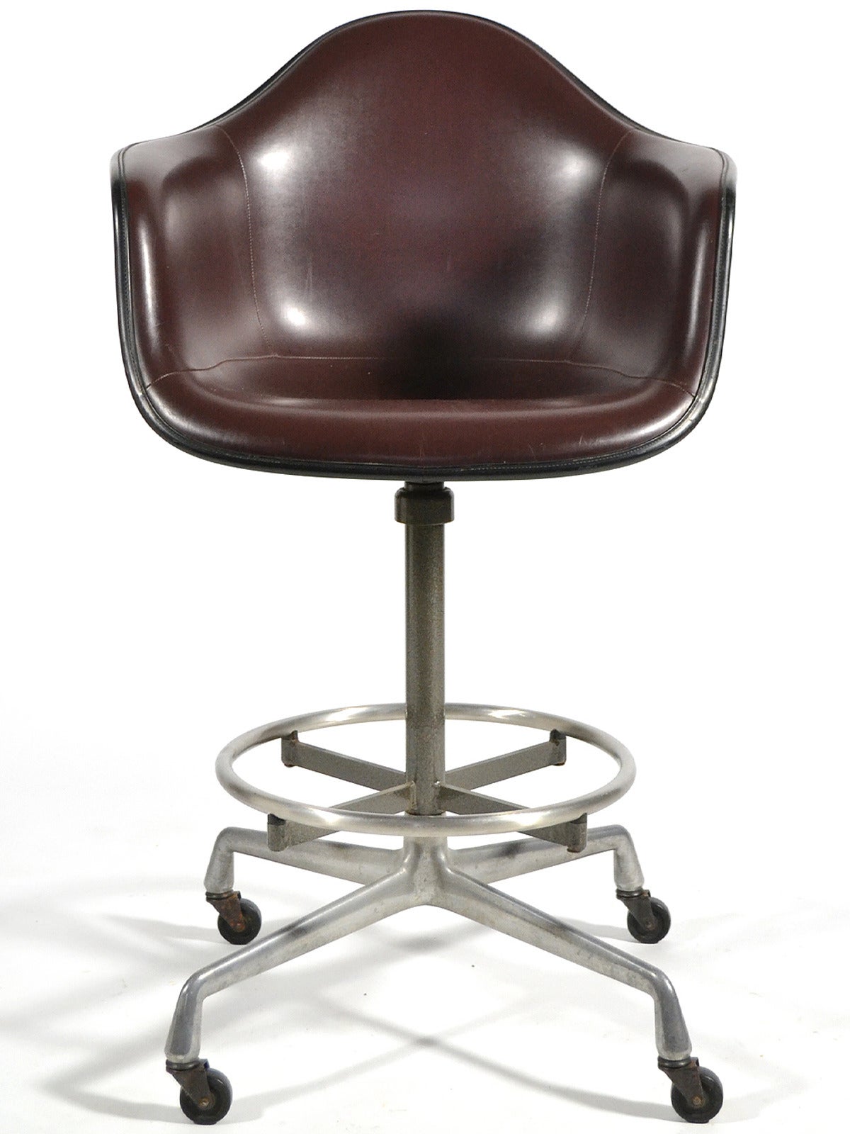 This Eames armchair features the uncommon drafting height base which has swivel function, adjustable height, and rolls on smooth casters. The armshell is of elephant hide gray fiberglass, with chocolate brown Naugahyde and black edge banding.