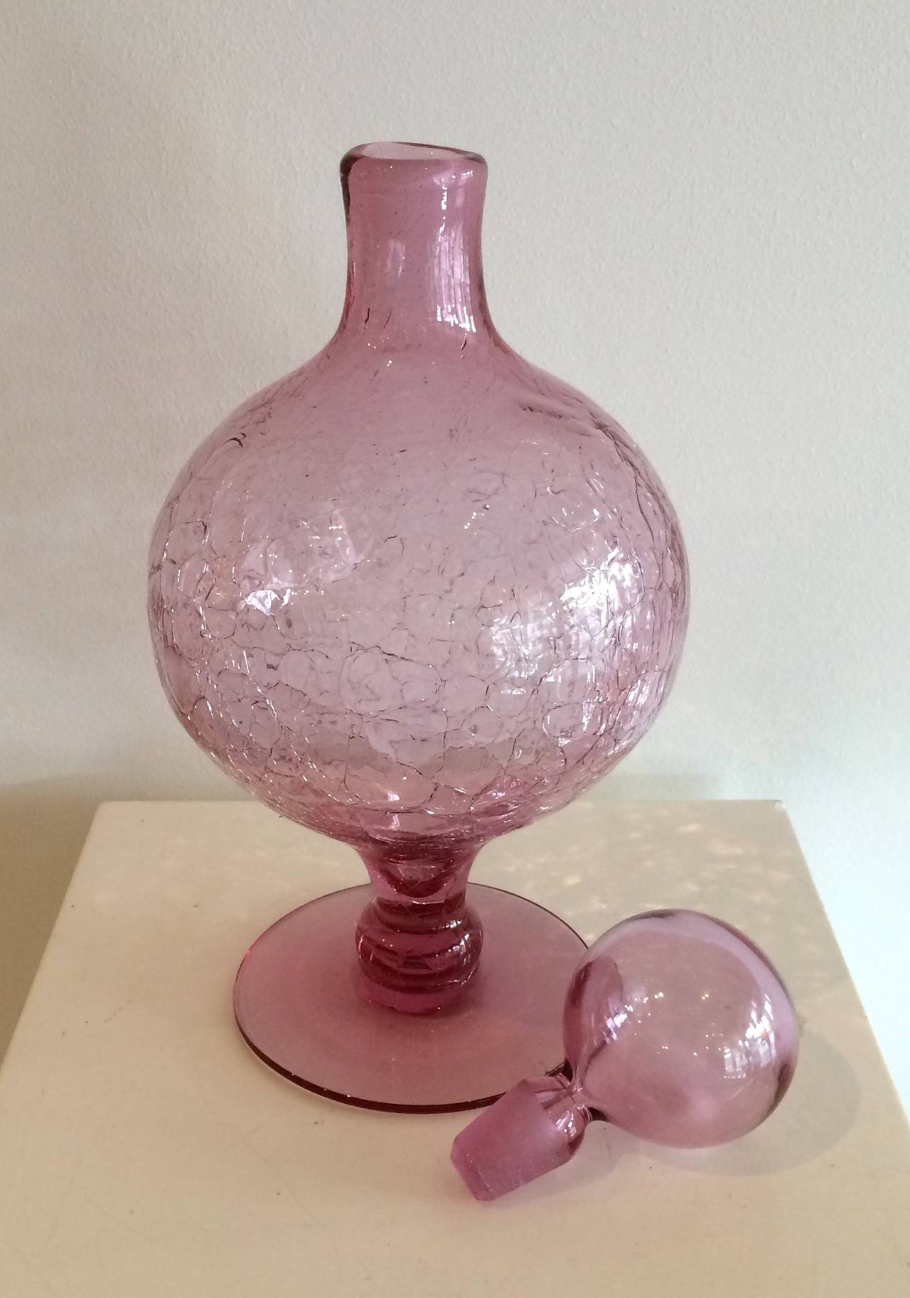 Light rose colored crackled glass decanter with round body and stopper.