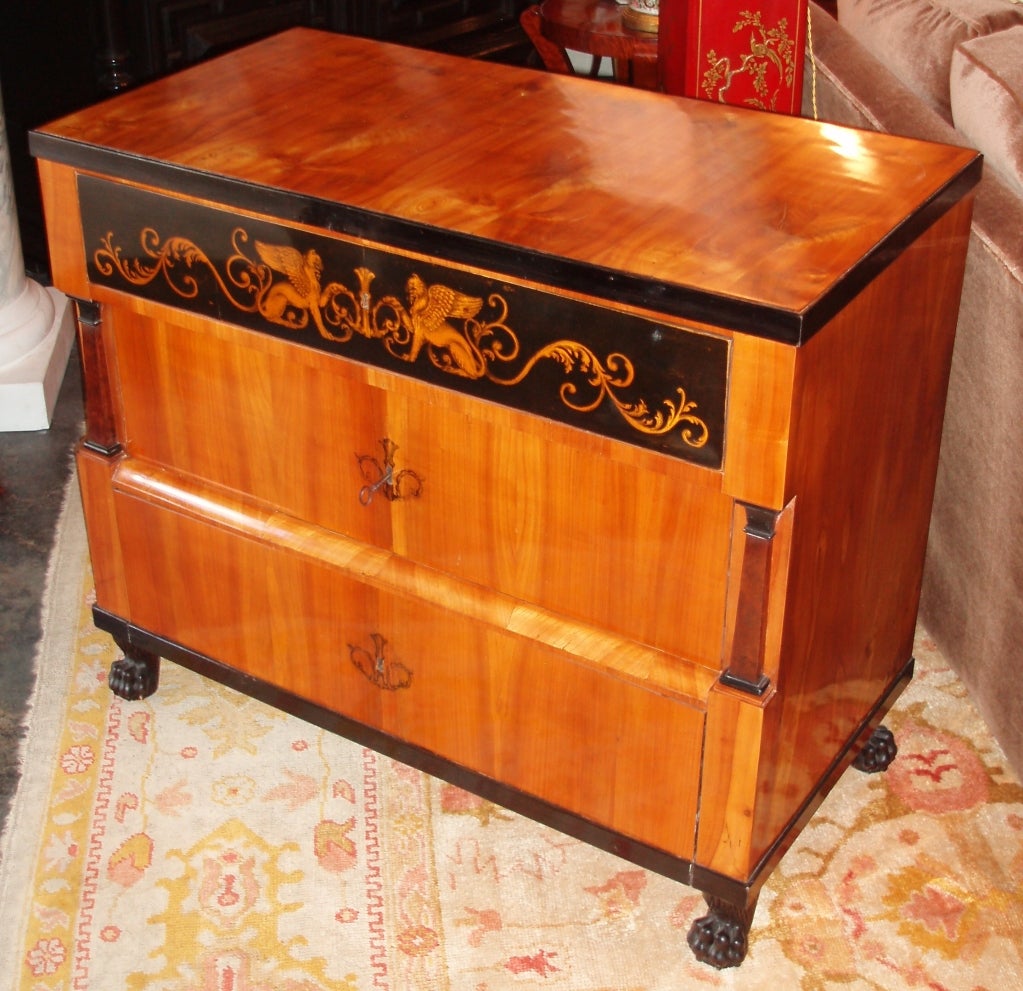 Commode Biedermeier en noyer poli avec garniture en ébène, illustration de deux griffons ailés de profil assis dans un motif décoratif d'acanthe flanquant le trou de serrure, trois tiroirs au total avec serrure et clé, et avec des motifs de colonnes