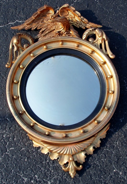 Handsome Regency style giltwood framed convex mirror crowned with spread eagle flanked by wing form mounts on opposing sides, set over a circular ebony inset frame with small ball mounted exterior border.