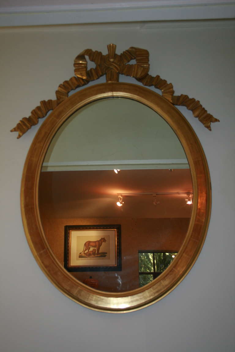 Lovely oval shaped giltwood framed mirror with carved and gilded tied ribbon bow at top center; French, 20th century.