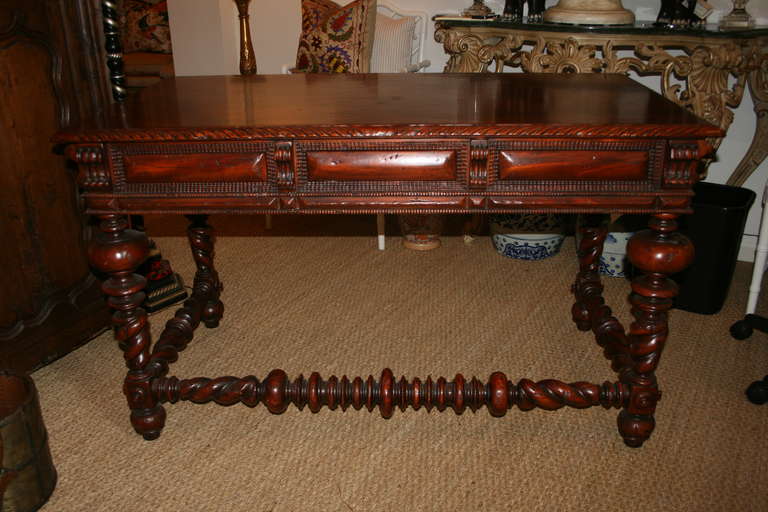 Portuguese style polished and carved wood library desk with circular and bulbous designed twist legs and front cross stretcher, top with carved beveled edge with three deep set drawers below.