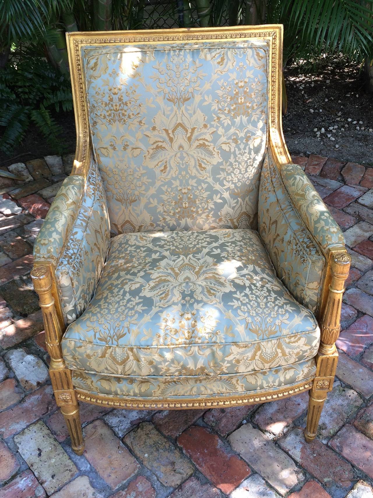 Carved giltwood bergere, upholstered in gold and blue silk fabric with floral motif.