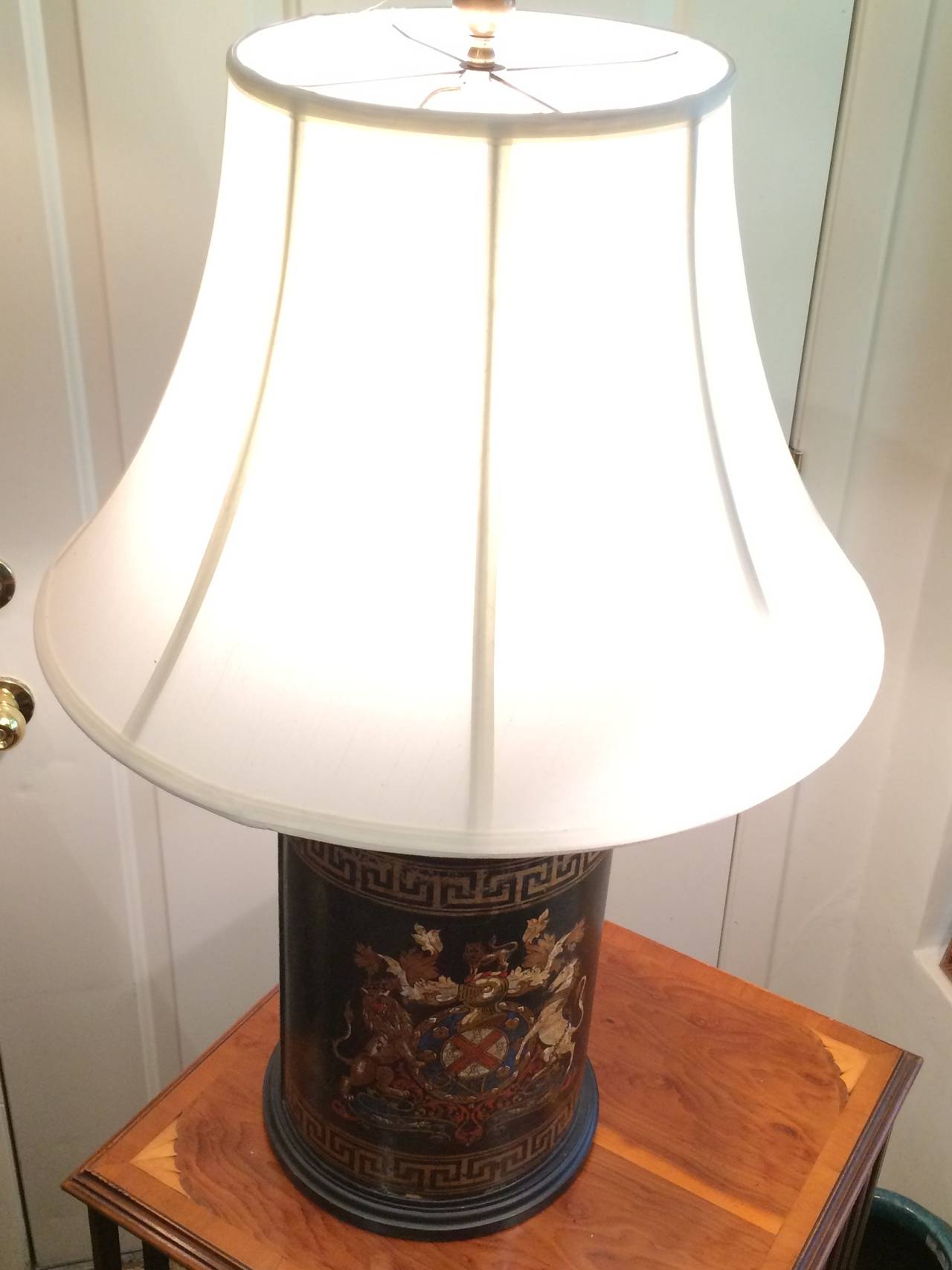 Antique Black painted tole canister mounted as lamp with handsomely illustrative English coat of arms motif and Greek key borders, early 20th century.
*Shade sold Separately.