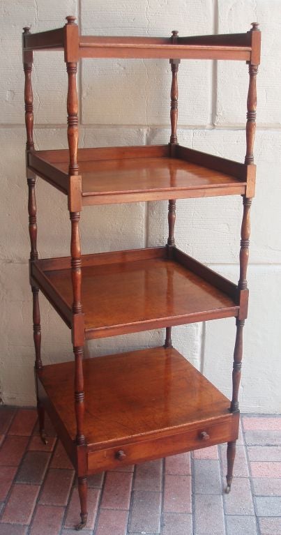 Handsome mahogany four shelved Regency etagere, square with single drawer beneath, on brass casters, smooth and carved stretchers connecting each level with three-sided slightly raised bordered walls on three of the shelves.