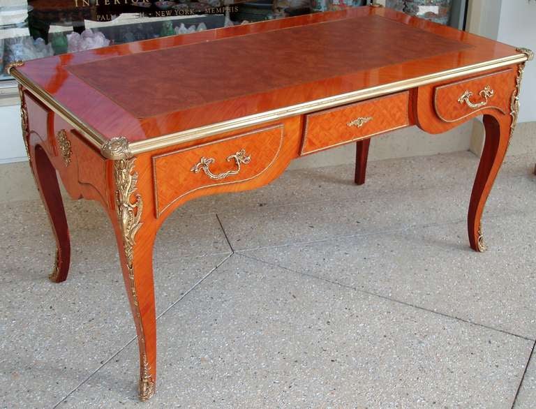 Séduisant bureau plat de style Louis XV, plateau en cuir tanné gaufré et doré, centré sur un beau panneau en placage de bois satiné et un cadre fini en marqueterie, fines moulures à motif Rocaille sur l'ensemble du plateau, un côté avec trois