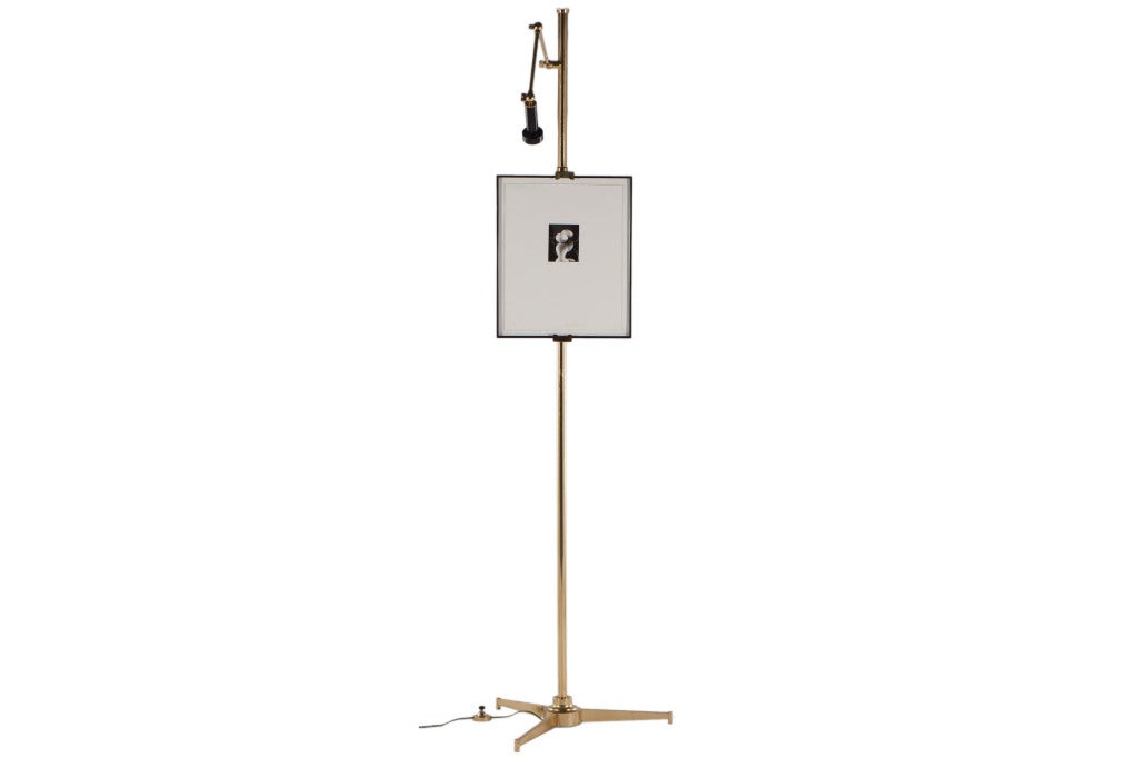 Easel lamp in brass with articulating arm with adjustable light. Also with adjustable easel. Early example with stepped base and crown shaped finial. Signed with decal to bottom