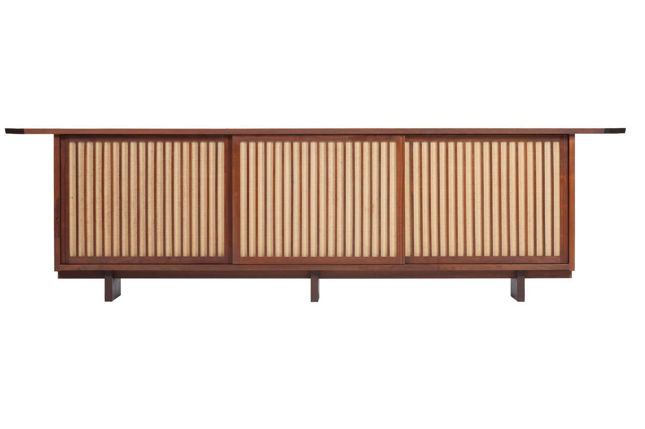 Extremely rare 10ft. George Nakashima triple credenza or sideboard in walnut circa 1959. Cabinet with 3 sliding doors with pandanus cloth, also with 2 compartments with shelves and one with drawers. Top with a free-edge and a double over-hang.