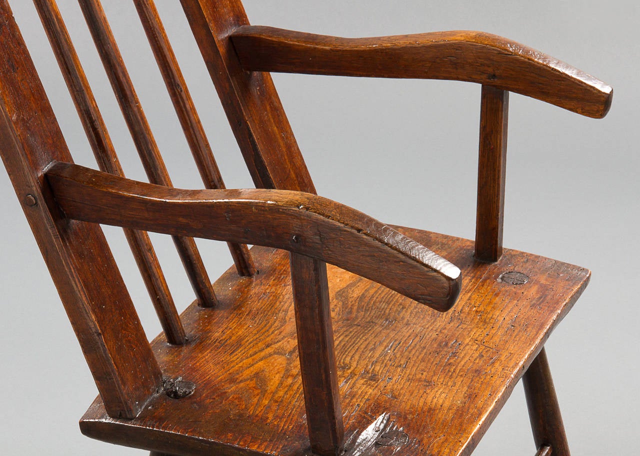 A late 18th century ash armchair with the back composed of three long spindles in a joined frame leading down to a plank seat, mortised with four splayed legs joined by front and back turned stretchers. The arms with interesting down-turned ends.