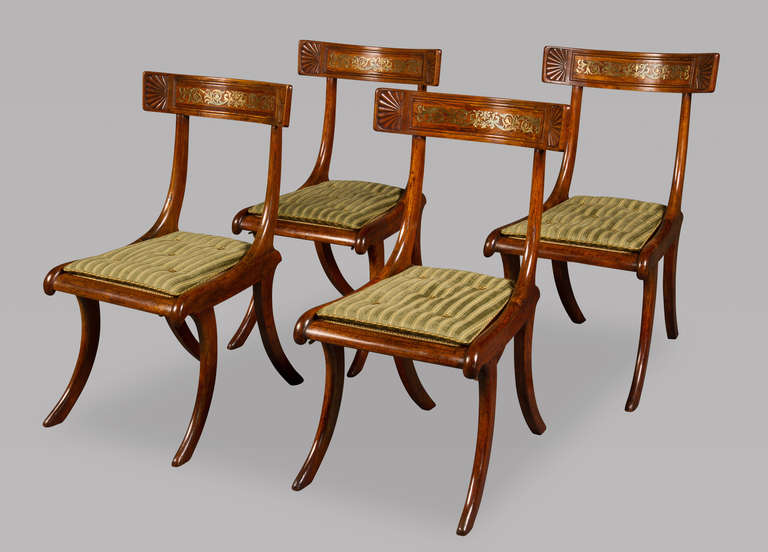 The deeply curved crest rails with carved palmettes to the sides anchored by brass inlay of trailing anthemion (honeysuckle). The seat caned and now with flat squab cushions above curved sabre legs to both front and back.

The chairs in beech and