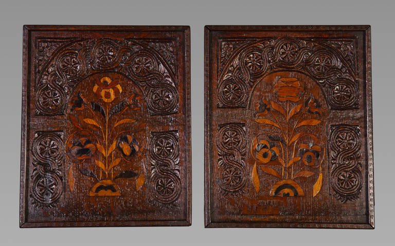 A pair of early 17th century oak panels. Each panel marquetried with floral designs beneath an arch enriched with carved flower-heads entwined in a guilloche band with leafy embellishments to the corners. The marquetry probably in sycamore and