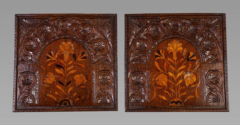 A pair of early 17th century oak panels. Each panel marquetried with floral designs beneath an arch enriched with carved flower heads entwined in a guilloche band with leafy embellishments to the corners. The marquetry probably in sycamore and