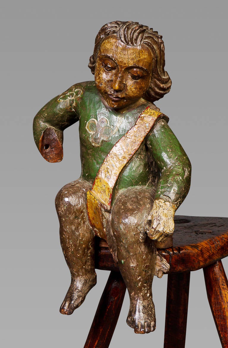 Originally from a larger piece, evidenced by the vacant mortise to the rear, the costume bandolier and stance of the subject may indicate a depiction of a boy soldier. The child wears a green coat emblazoned with a stylized four-leaf clover. The